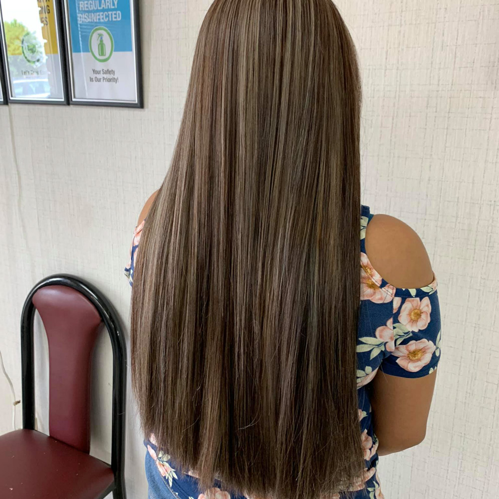 A back view of a client with exceptionally long, straight hair featuring a multi-tonal ash brown and blonde balayage. The hair shows off a healthy, high-shine finish and a blunt cut at the ends, highlighting the professional hair coloring and silk press services available at Beauty Town Salons.