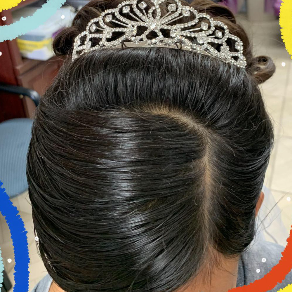 A close-up overhead view of a sleek, dark brunette formal updo featuring a polished French twist and a shimmering silver rhinestone tiara. The hair is styled with a smooth, glossy finish, showcasing the intricate folding technique used by the stylists at Beauty Town Salons for weddings or prom.